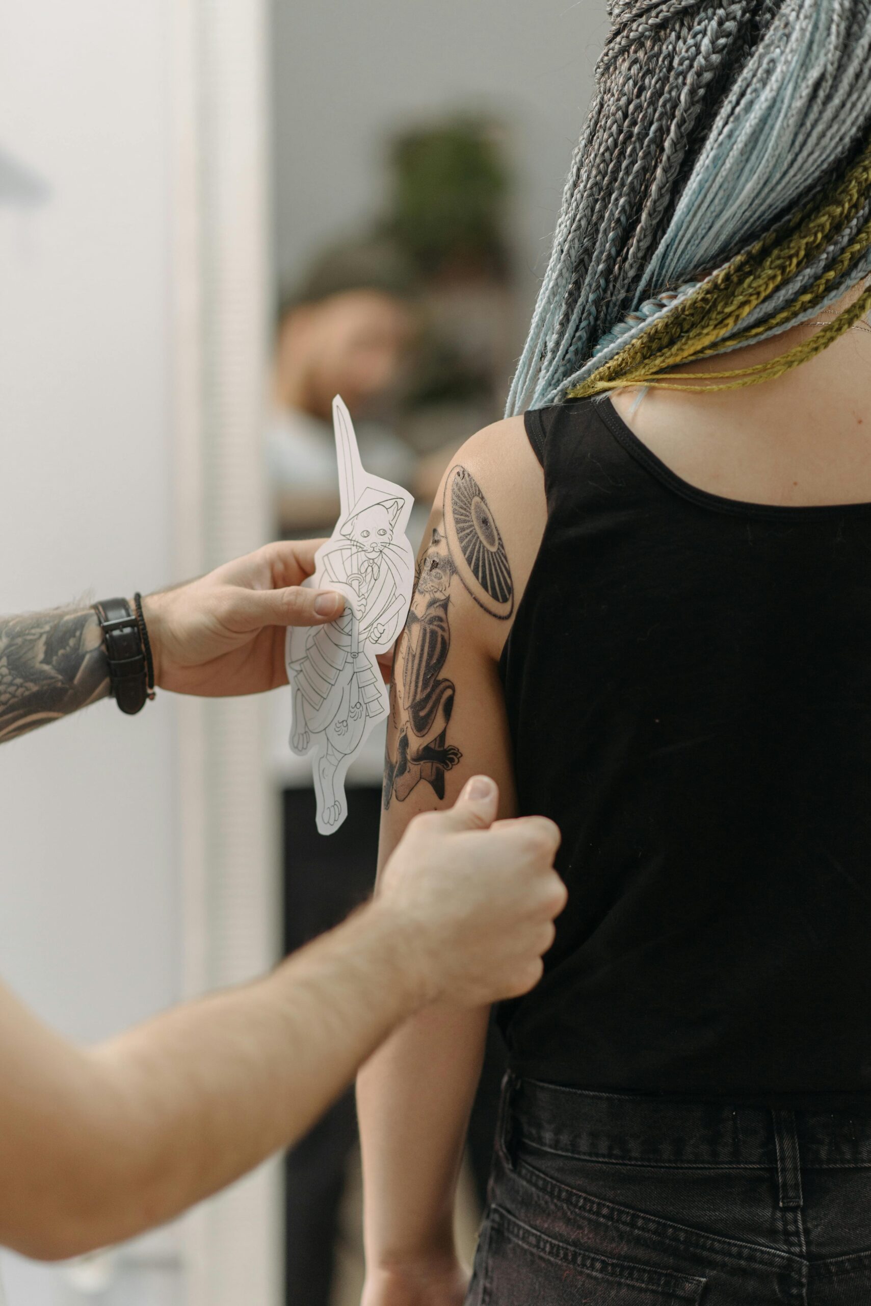 Tattoo artist prepares to place design on a woman's upper arm indoors.